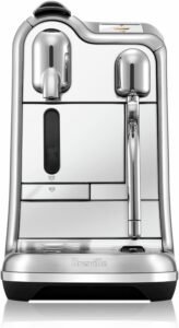 "A brushed stainless steel Nespresso machine with a 1500-watt power output. It features a color touchscreen display, built-in milk frother, and multiple customizable beverage options."