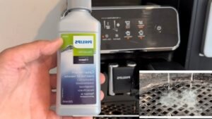 "Hand holding a bottle of Philips descaler in front of a Philips coffee machine, with an inset showing the descaling process."