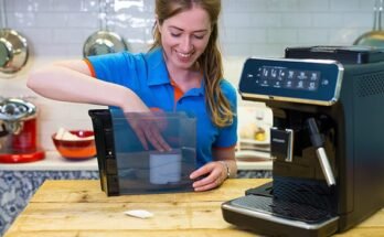 "Smiling woman in a blue shirt placing a water filter into the reservoir of a Philips coffee machine on a wooden countertop in a modern kitchen."