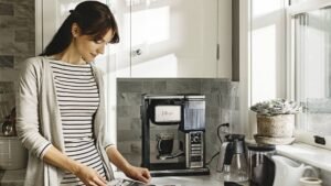 Image of a women stands close to the shelf where there is a ninja espresso producer .